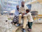 A man, a woman and a small boy sit outside a crowded shelter building at a camp for displaced people in Mekelle, Tigray