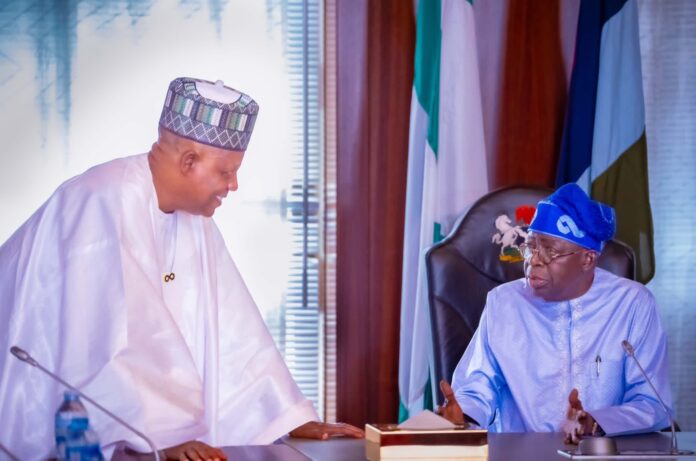 President Bola Tinubu seated at right speaking with Vice President Kashim Shettima, who leans in from the left