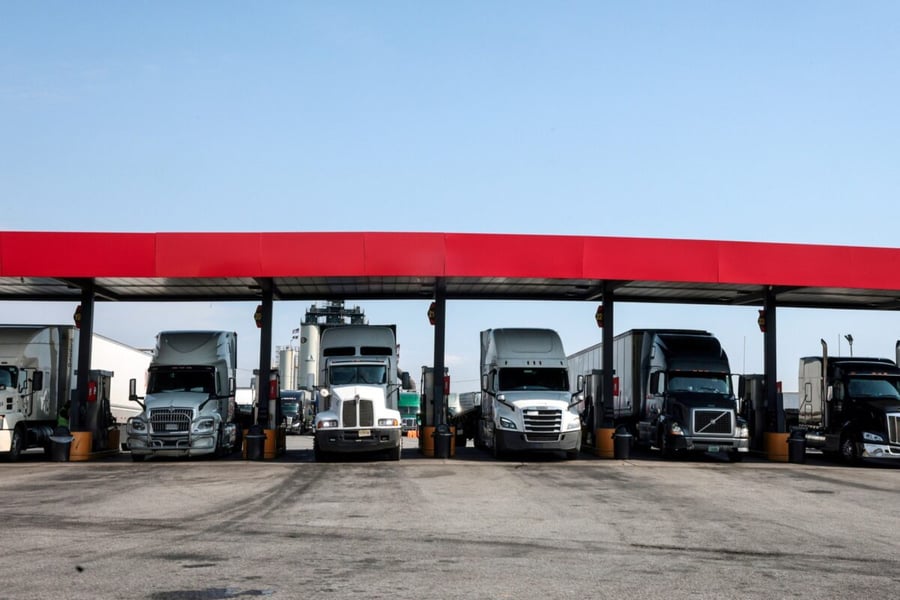 A row of semi trucks parked under a red canopy at a truck stop fuel island