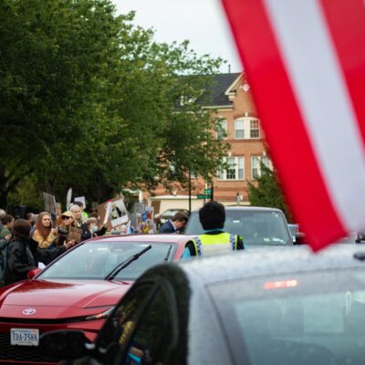 Demonstrators with signs outside Trump National Golf Club as cars arrive for the first meme coin dinner