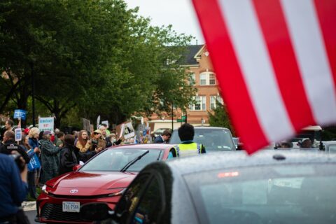 Demonstrators with signs outside Trump National Golf Club as cars arrive for the first meme coin dinner