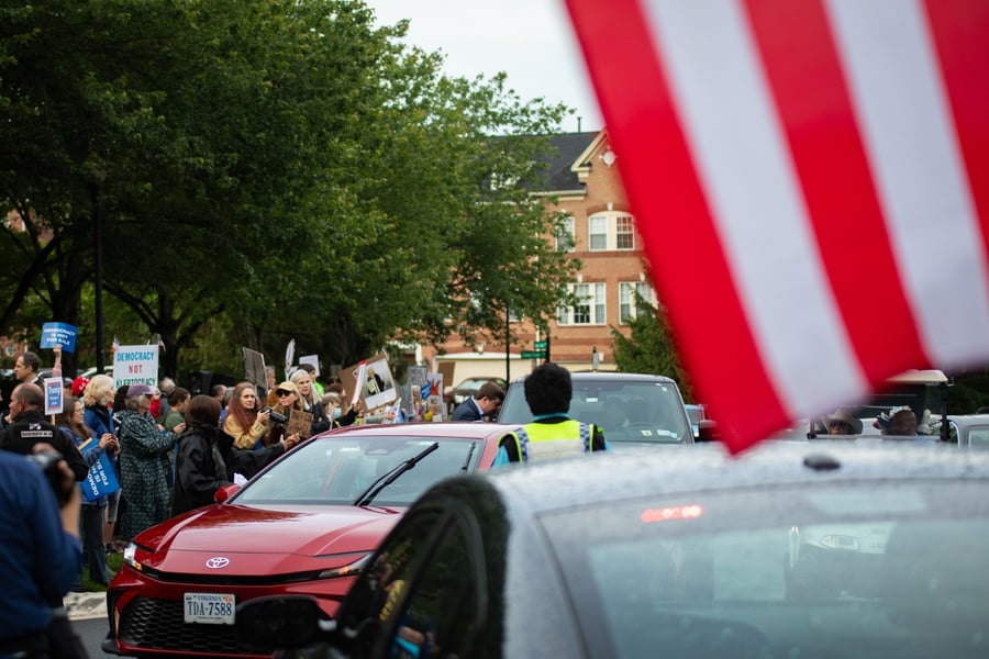 Demonstrators with signs outside Trump National Golf Club as cars arrive for the first meme coin dinner
