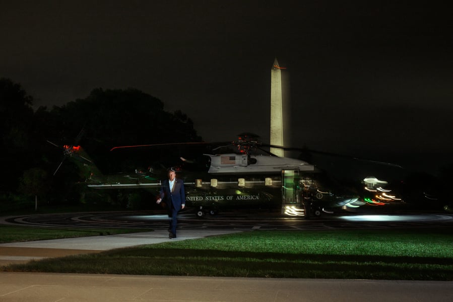 President Trump walks across the South Lawn at night in front of Marine One, with the Washington Monument lit behind