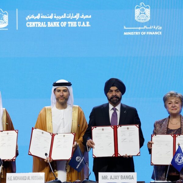 Four officials hold open signed agreement folders on stage in front of a blue backdrop at the 2029 Annual Meetings signing in Bangkok
