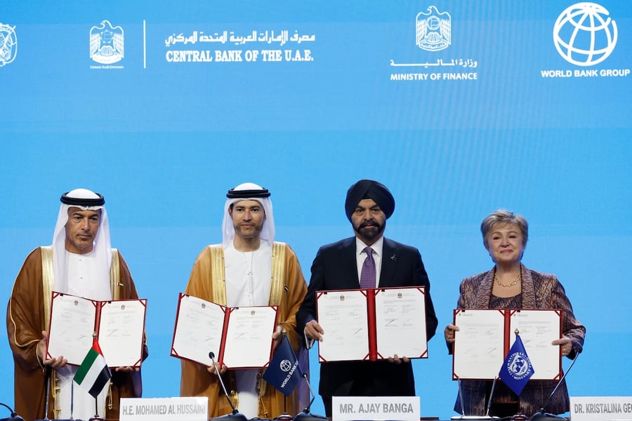 Four officials hold open signed agreement folders on stage in front of a blue backdrop at the 2029 Annual Meetings signing in Bangkok