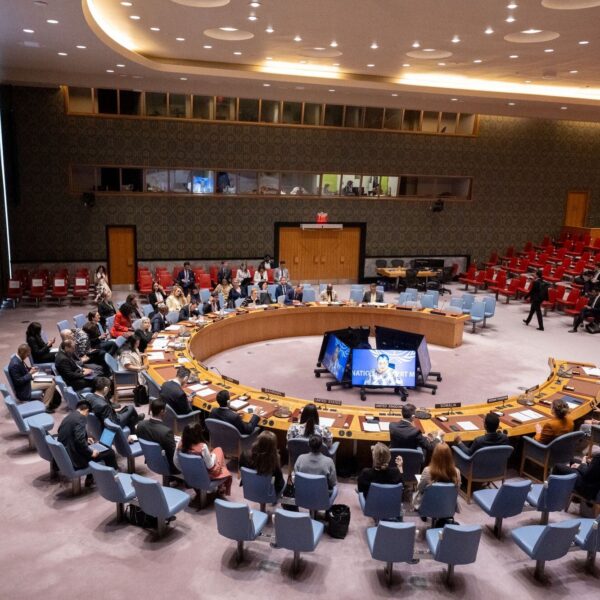 Security Council members sit around the horseshoe table in the chamber while a large screen shows the UN envoy briefing by video link