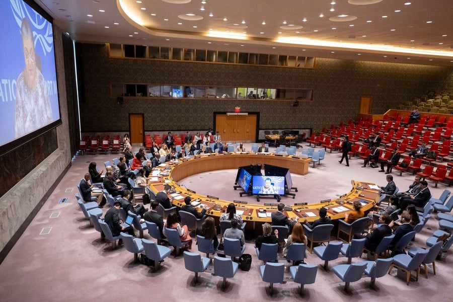 Security Council members sit around the horseshoe table in the chamber while a large screen shows the UN envoy briefing by video link