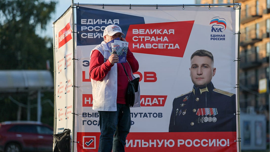 A campaigner holding leaflets in front of a United Russia election banner in Moscow