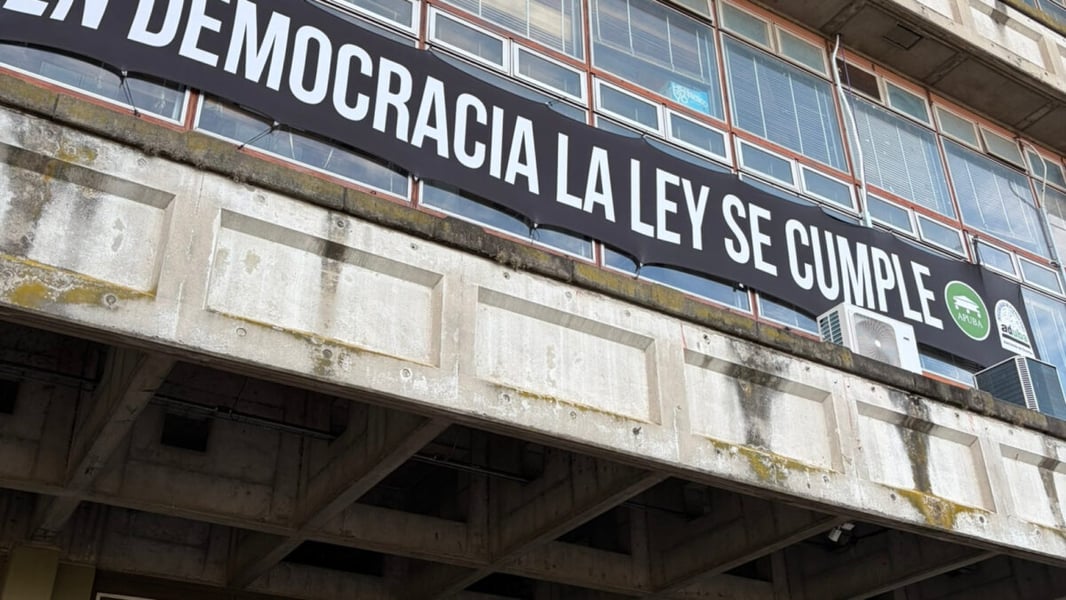 Black banner with white letters reading En democracia la ley se cumple hangs across the concrete facade of a university building in Buenos Aires