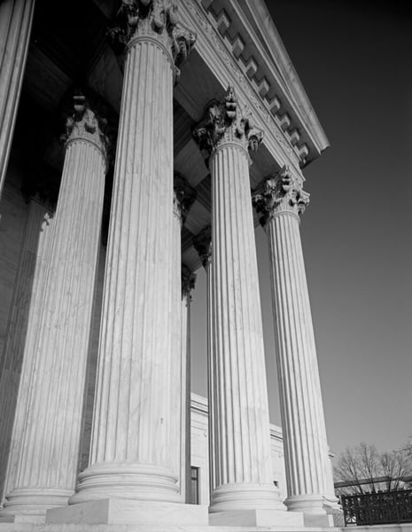 Black-and-white view looking up at the marble columns and cornice of the U.S. Supreme Court building