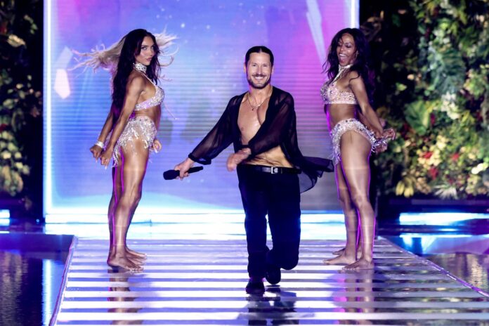 Val Chmerkovskiy walking a runway between two dancers at the Sports Illustrated Swimsuit Runway Show in Miami Beach