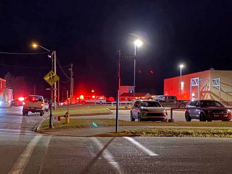 Emergency vehicles with flashing red lights on a street corner near Wainwright High School at night