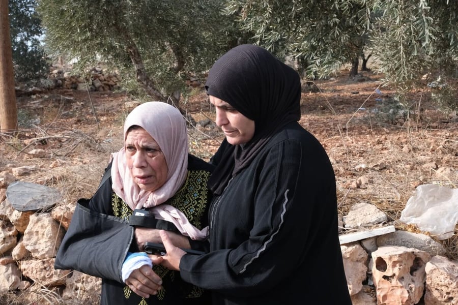 A relative holds Warda Adeli, 63, whose arm is in a sling, in front of olive trees in the West Bank village of Usarin