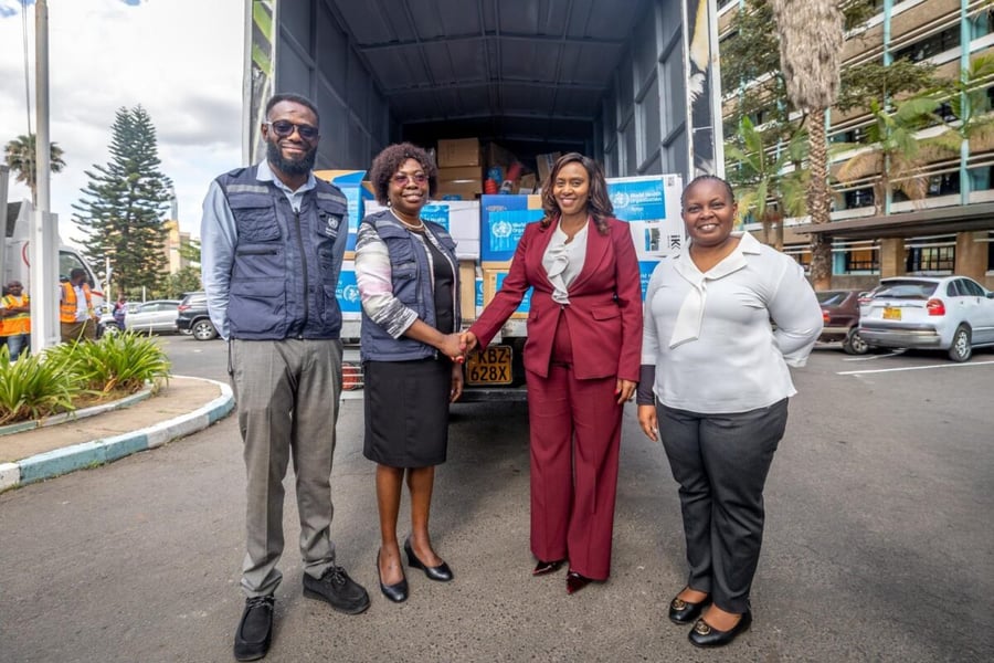 Four officials stand beside a truck loaded with WHO-marked boxes of Ebola response supplies in Nairobi