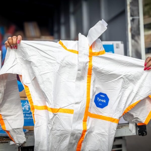 A person holds up a white protective coverall with orange tape from the back of a delivery truck