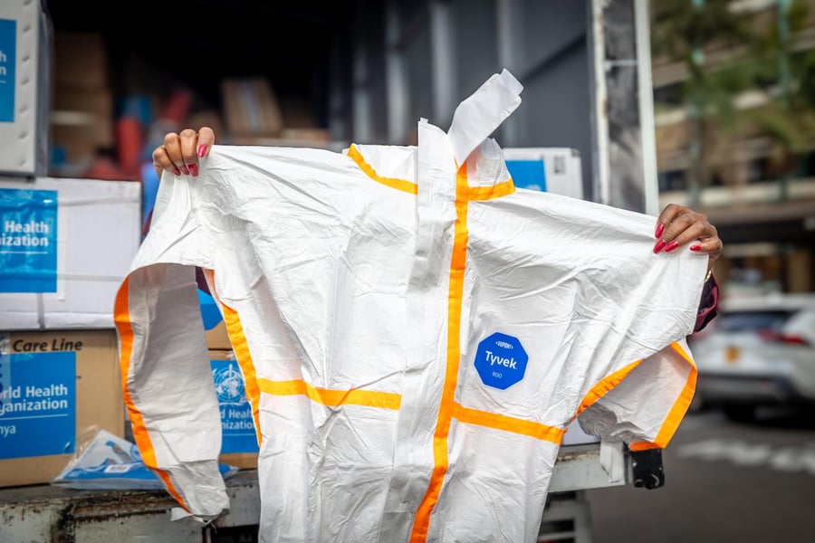 A person holds up a white protective coverall with orange tape from the back of a delivery truck