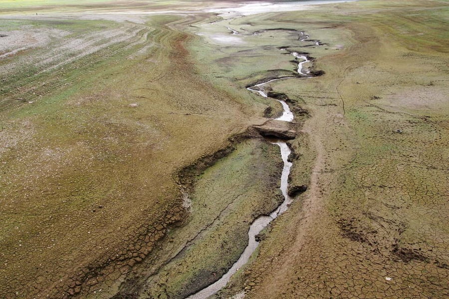 Aerial view of the cracked, exposed bed of Wimbleball Reservoir in Somerset with a narrow stream running through it