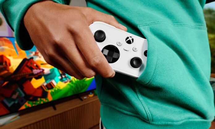 Person holding a white Xbox Nano Controller with a game displayed on a television behind them.