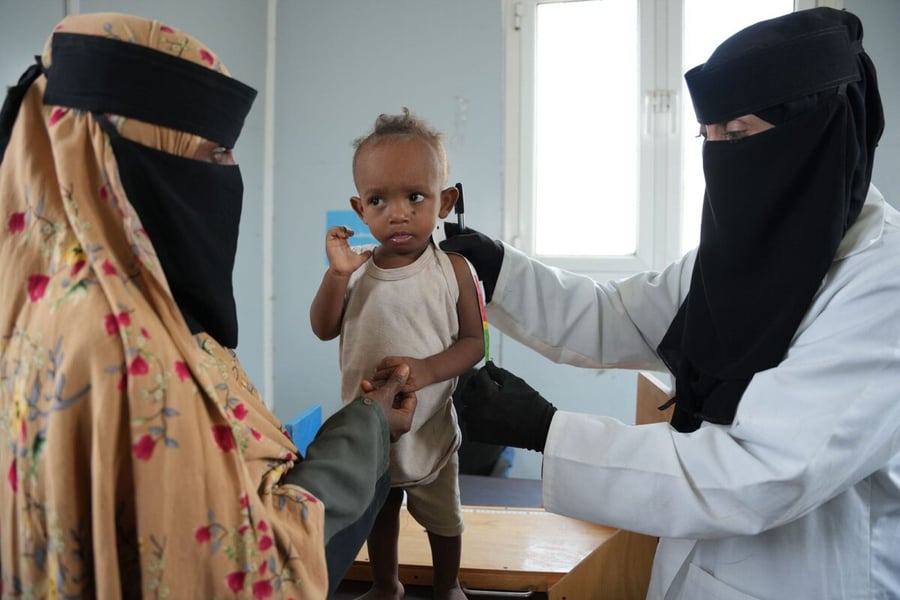 A health worker measures a young boy's arm to screen for malnutrition at a clinic in Aden while his mother holds him