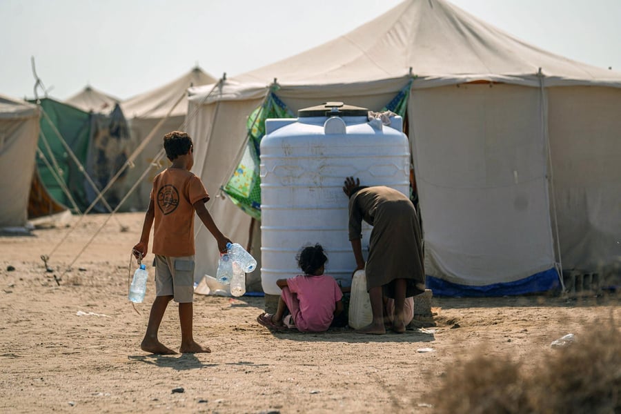 Displaced children and a woman collect water from a storage tank at a displacement camp in Yemen