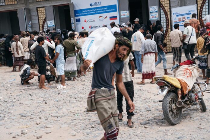 People collect food from a WFP emergency distribution centre in Lahj, Yemen, a man carrying a sack of milled rice