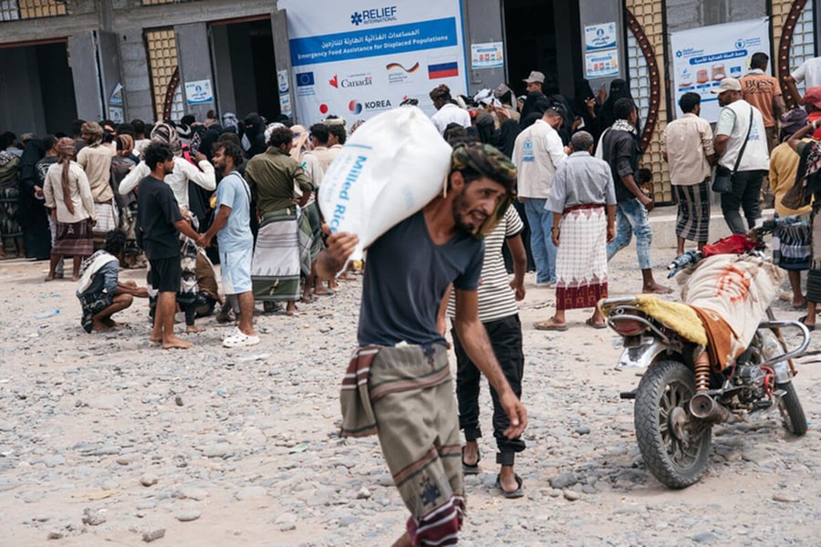 People collect food from a WFP emergency distribution centre in Lahj, Yemen, a man carrying a sack of milled rice