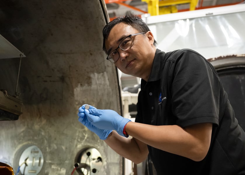 Yi Lin of NASA Langley holds a small coin-cell battery beside a thermal vacuum chamber after testing